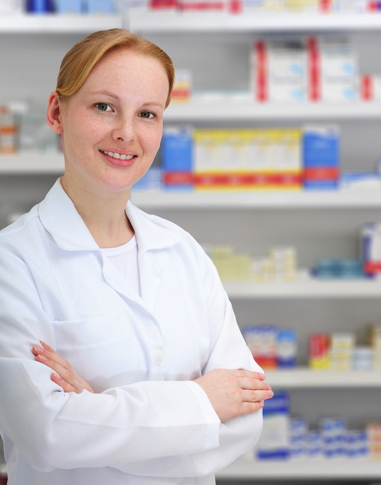 A pharmacist stands proudly in front of a medicine shelf.